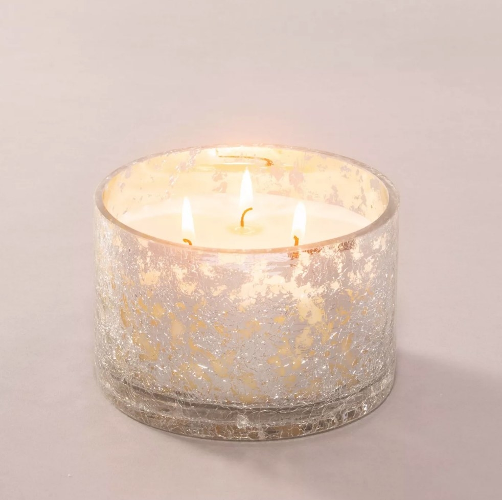 White three wick candle burning in silver foiled jar