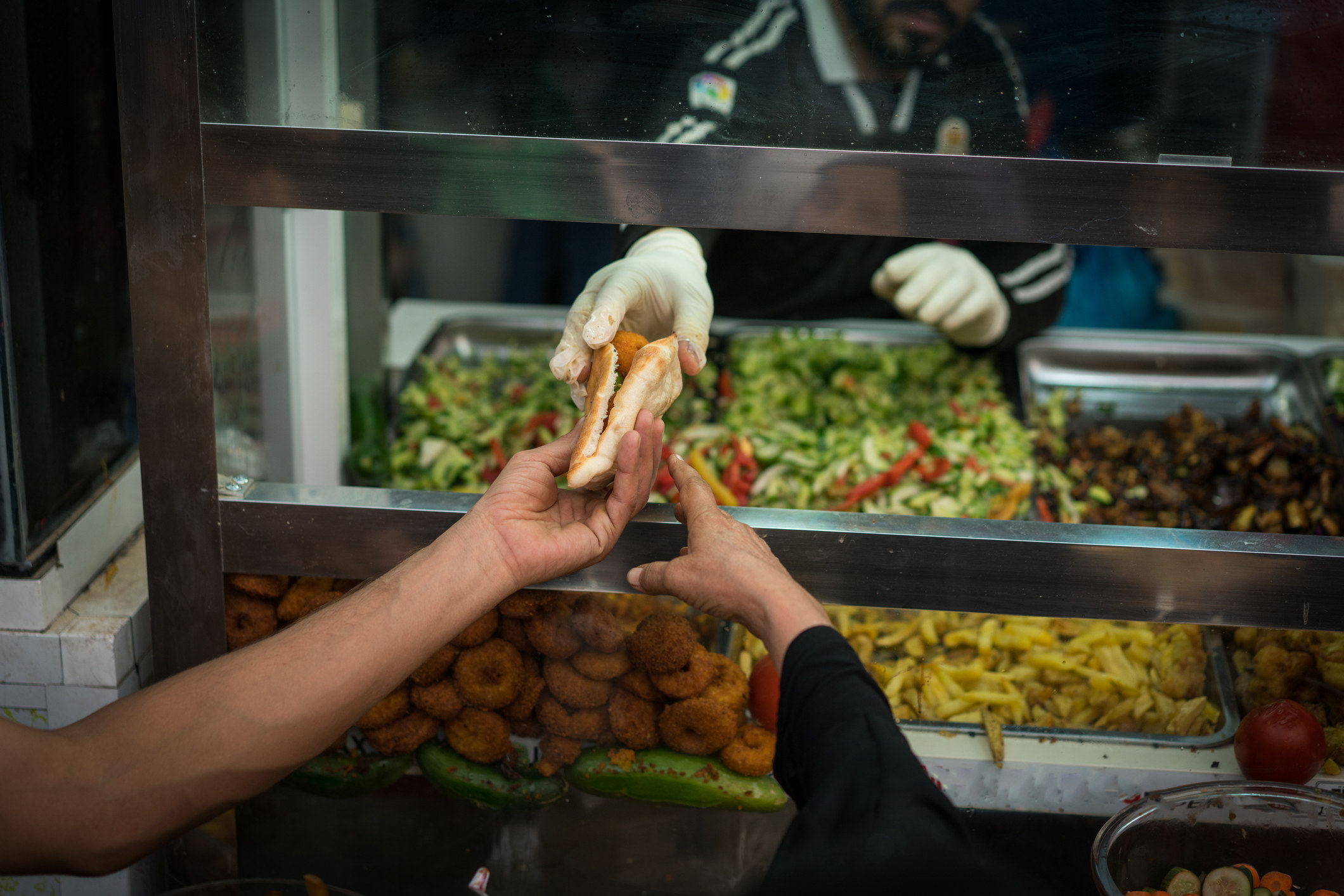A street vendor handing a falafel pita.