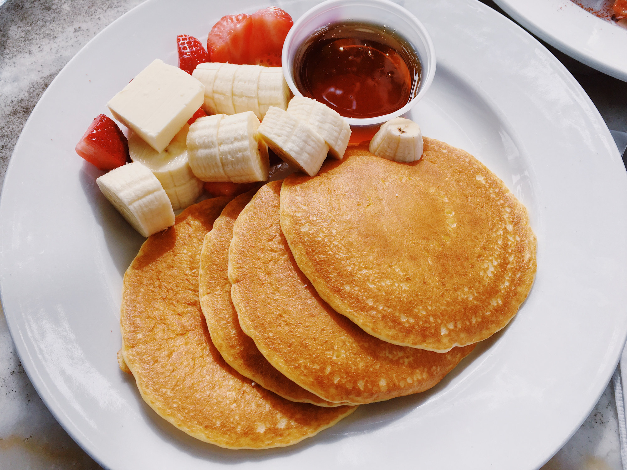 Pancakes on a plate with banana, strawberry and maple syrup.