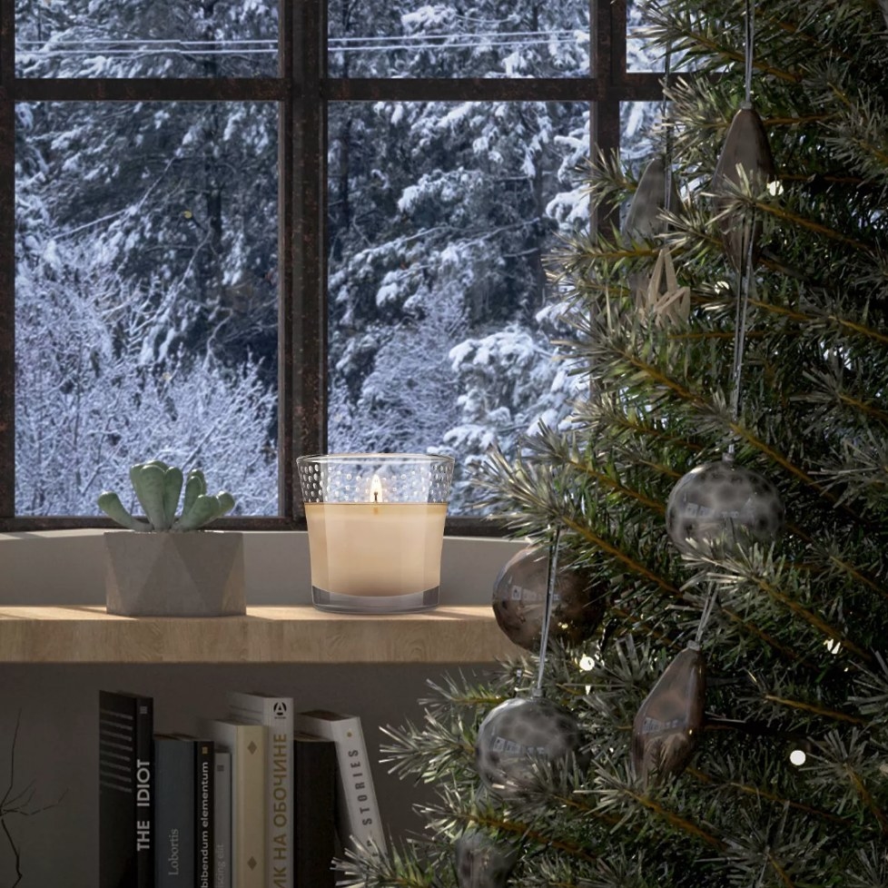 White candle in glass sitting on window sill behind christmas tree