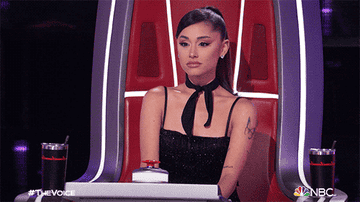 Ariana Grande sits in and chair and closes her eyes as she shakes her head quickly in &quot;The Voice&quot;
