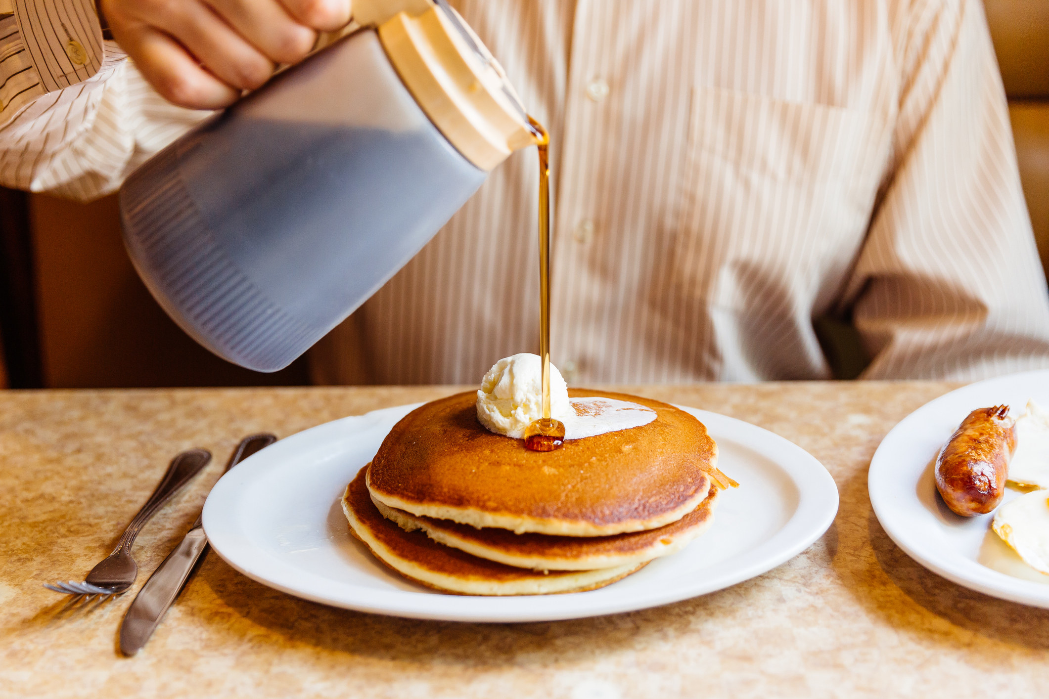 Pouring maple syrup onto a stack of pancakes.