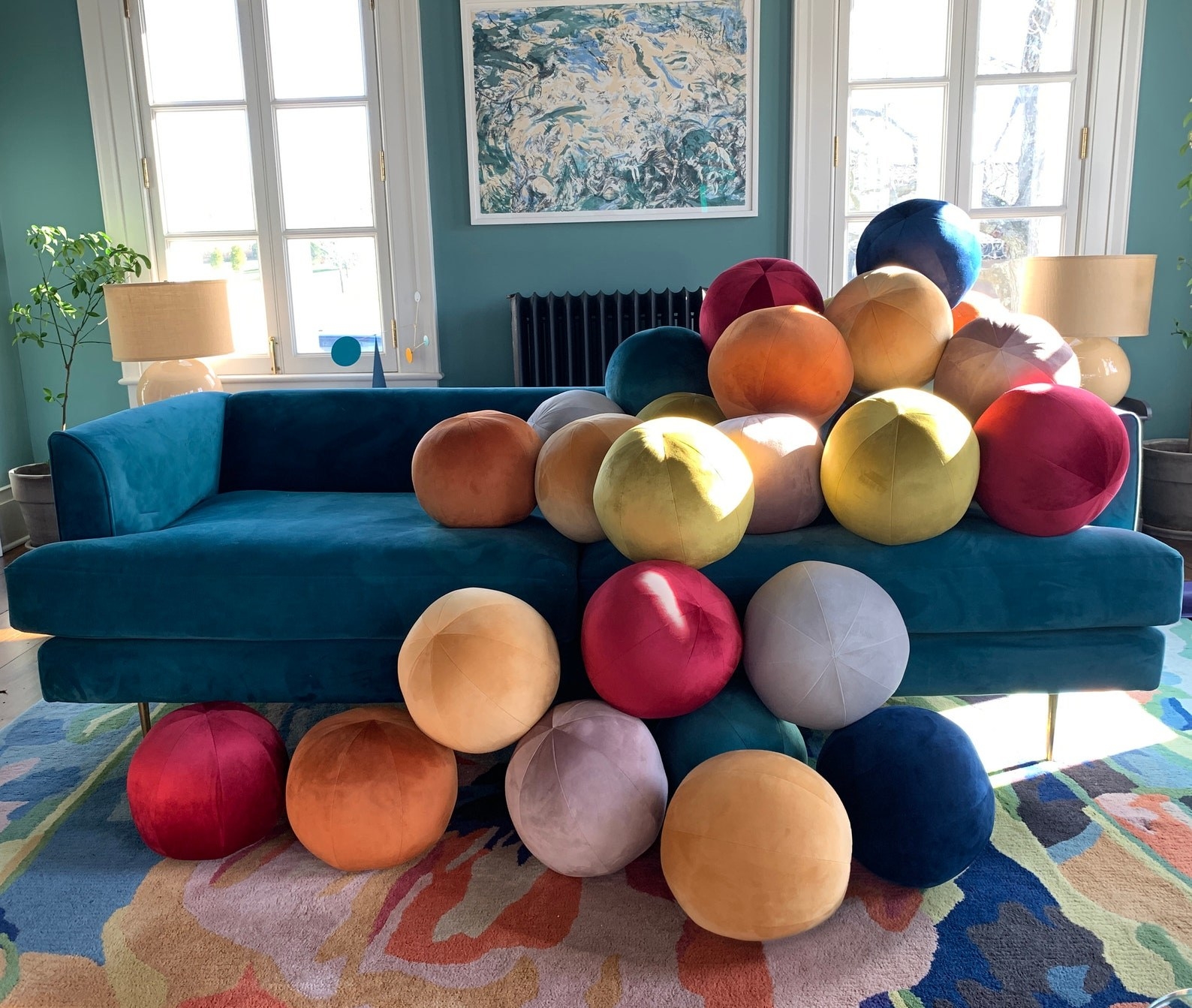 A variety of the velvet ball pillows in different colors piled onto a sofa