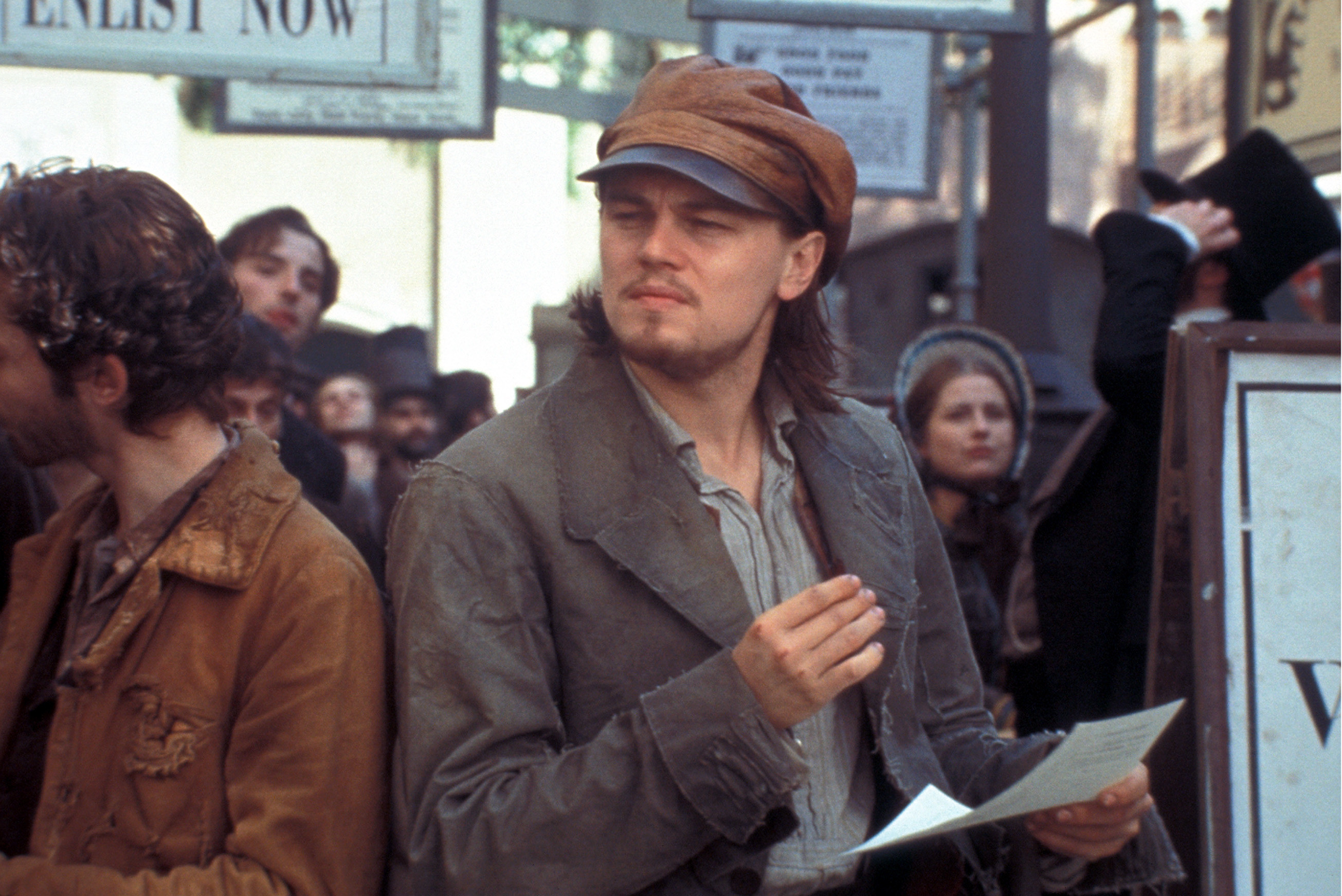Leonardo DiCaprio wears a dirty hat and stands in a crowd