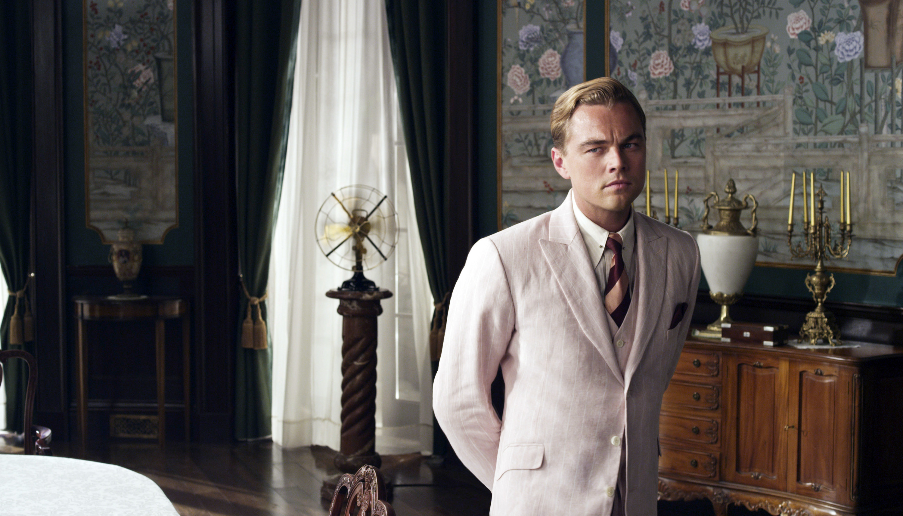Leonardo DiCaprio stands in a pink suit in a room with beautiful wallpaper