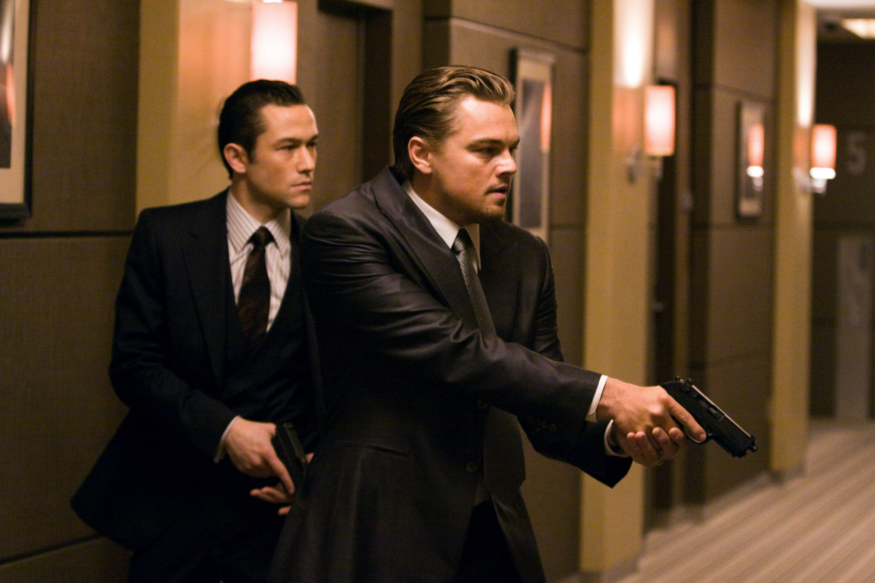 Joseph Gordon-Levitt and Leonardo DiCaprio walk down a hallway with guns