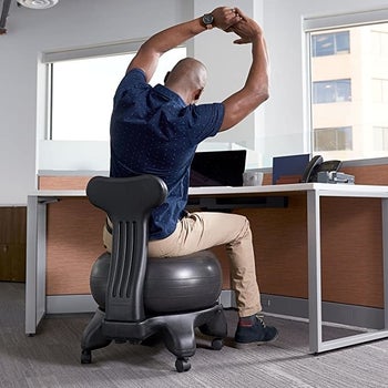 Model stretching on black exercise ball chair in an office