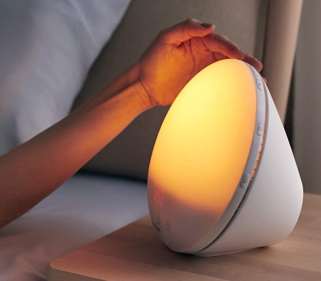 a person touching the top of the sunrise alarm clock