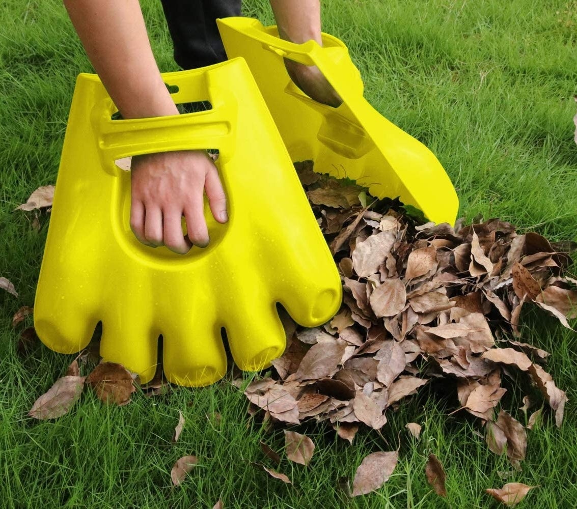 A person cleaning up a pile of leaves with the scoops