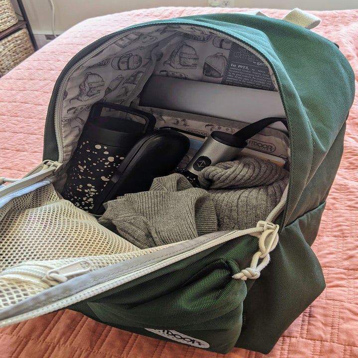 a reviewer image of the open backpack filled with a laptop, book, water bottle, umbrella, and cardigan
