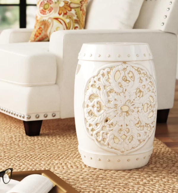 A round drum-shape ceramic garden stool with open floral designs. Includes nailhead dots around the top and bottom and has a flat top.