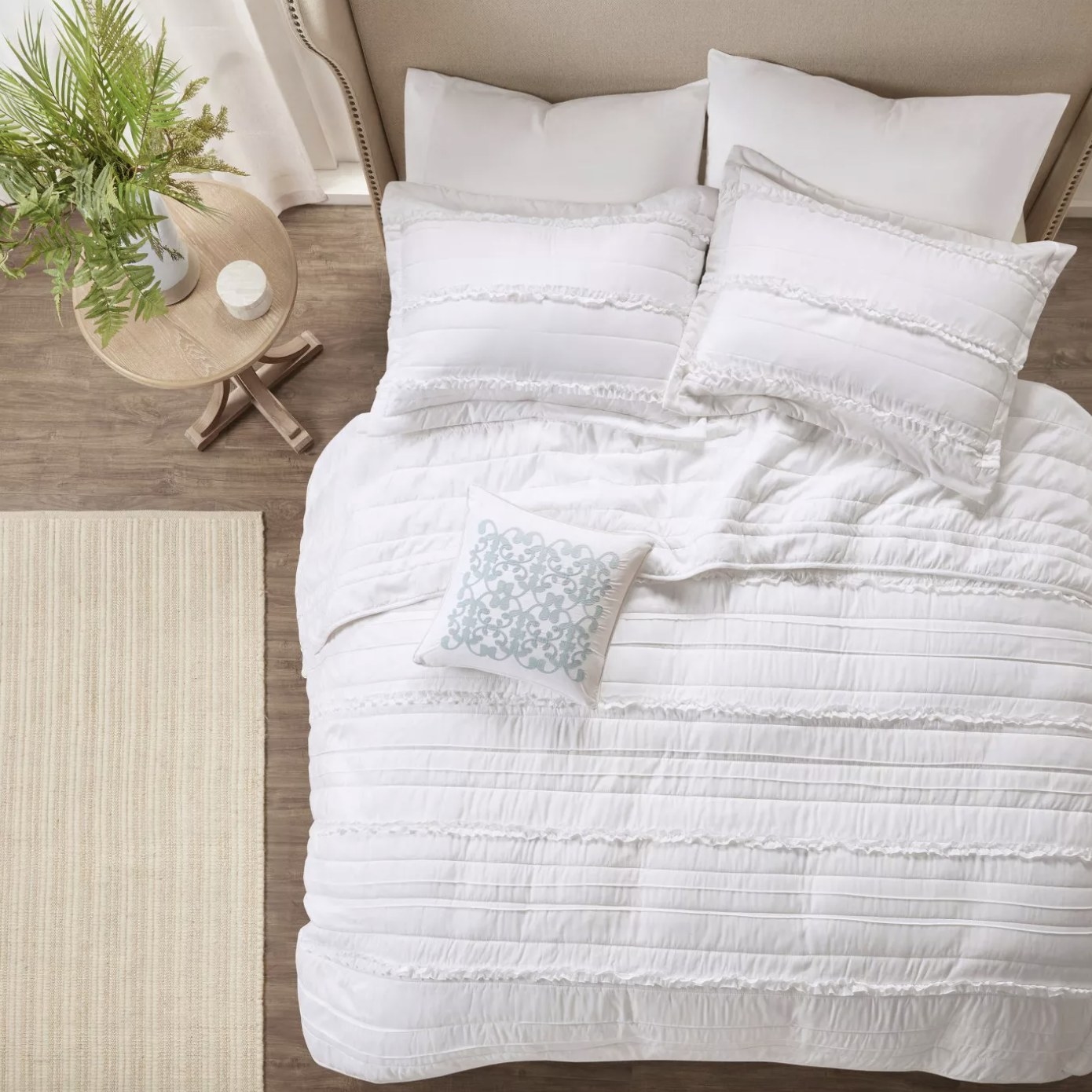 The white comforter has multiple vertical stitches, ruffles and a embroidered pillow