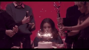 Girl sitting and sadly looking at her sparkler birthday cake while people celebrate