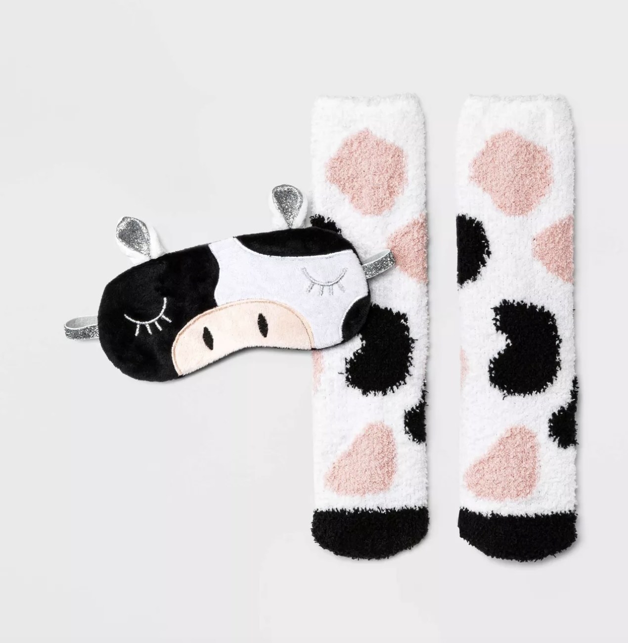 The cow mask has a sleepy face with pink, white, black and silver detailing and the socks have pink and black cow spots