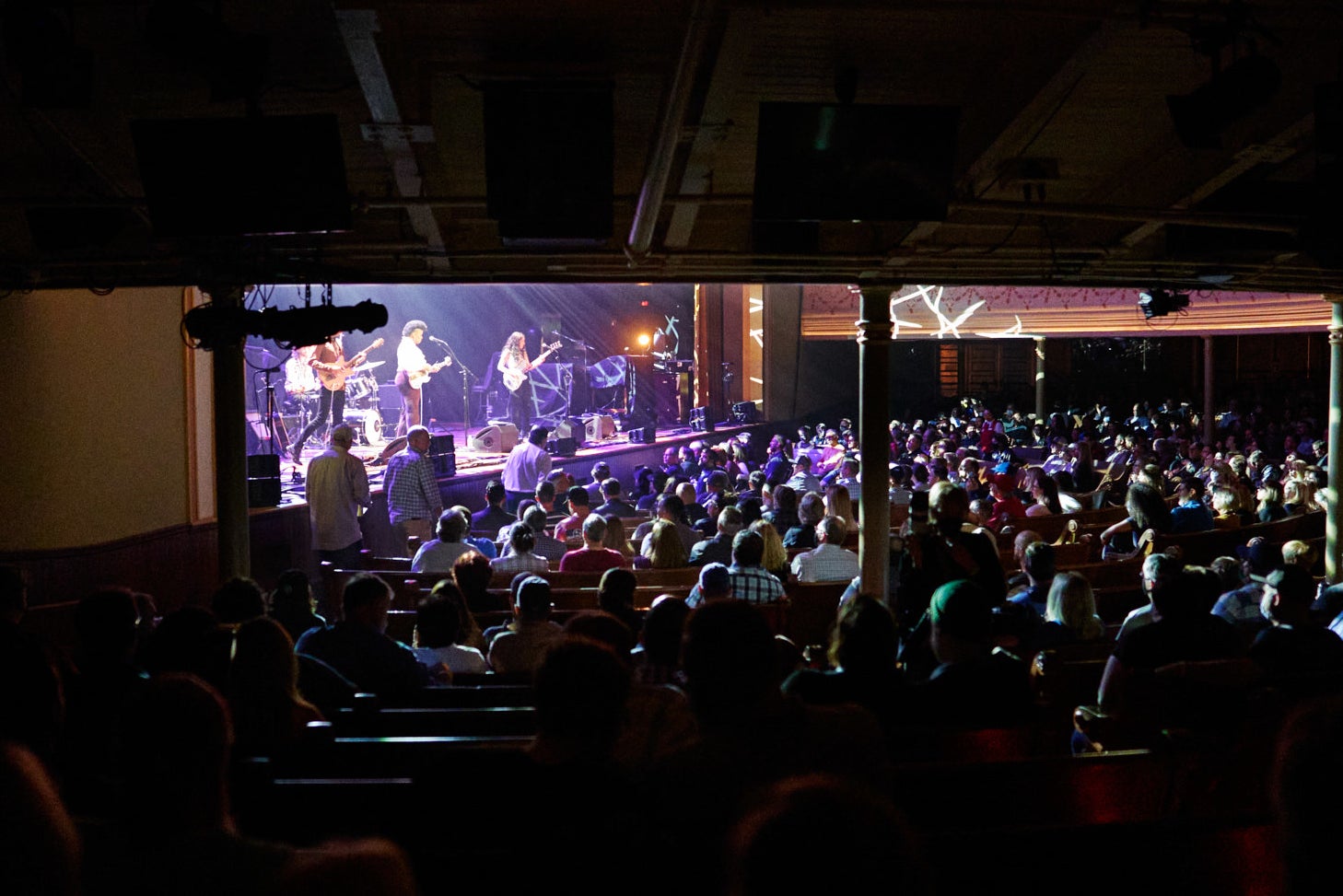 A packed crowd standing in pews watches a band perform onstage