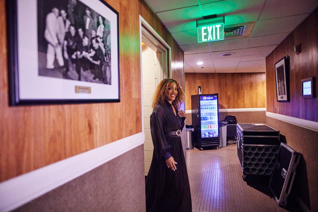 A grinning woman stands in a doorway in a backstage hallway