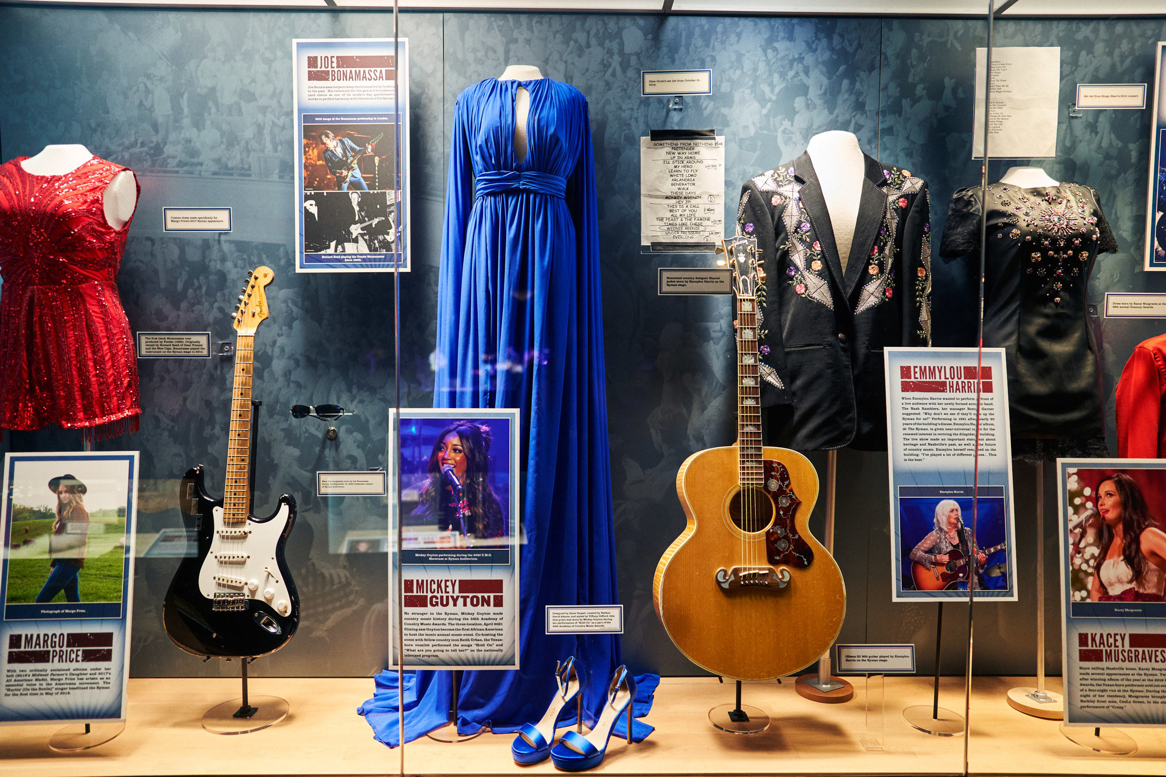 A dress is on display behind glass, between guitars and other outfits worn by artists who performed at the venue
