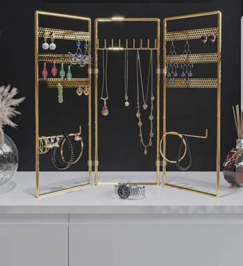 the gold frame organizer with three panels, one with hooks for necklaces and the other with holes for earrings and bracelet hooks