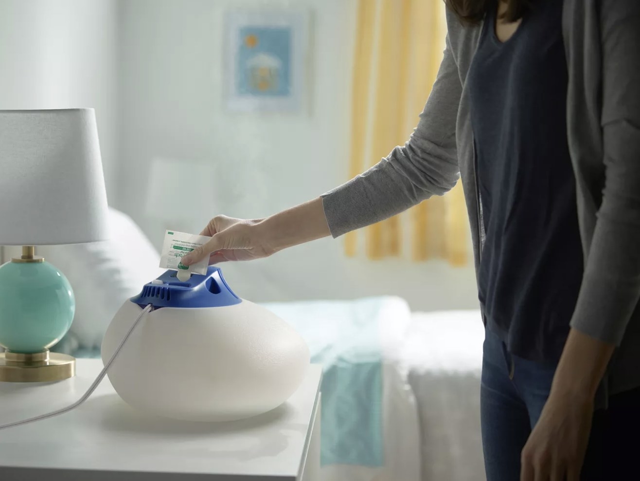 An adult pours a packet into the blue top of the pearly colored humidifier