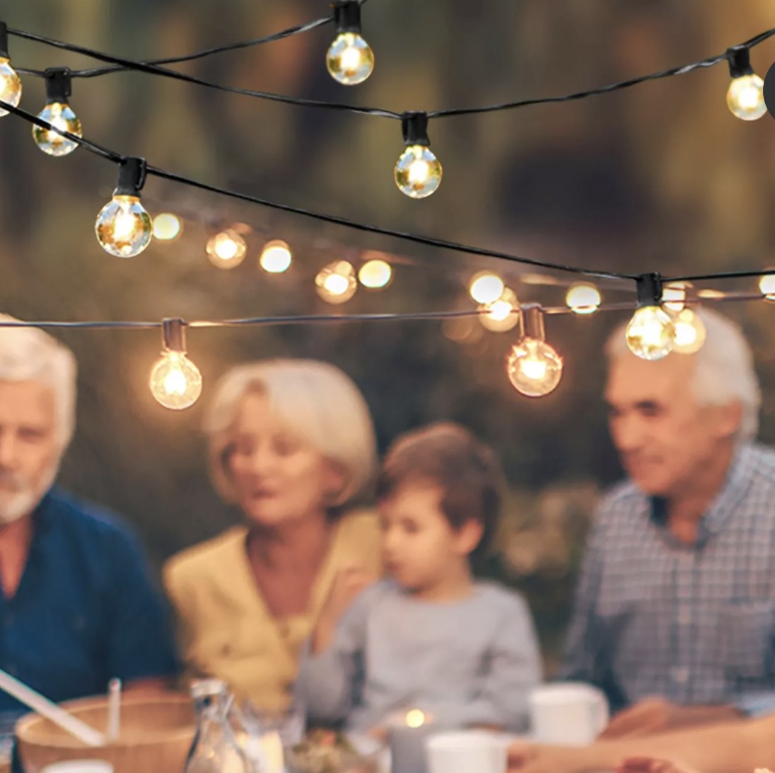 A few adults and a child sit outside under lit up string lights