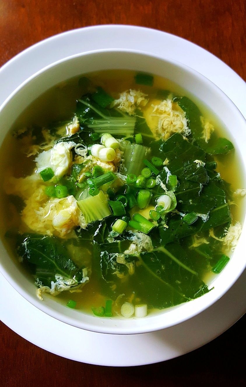 A bowl of egg drop soup with green vegetables.