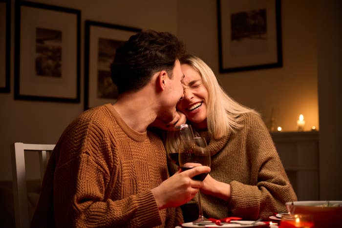 A man and a woman sitting at the dinner table laughing and holding wine glasses