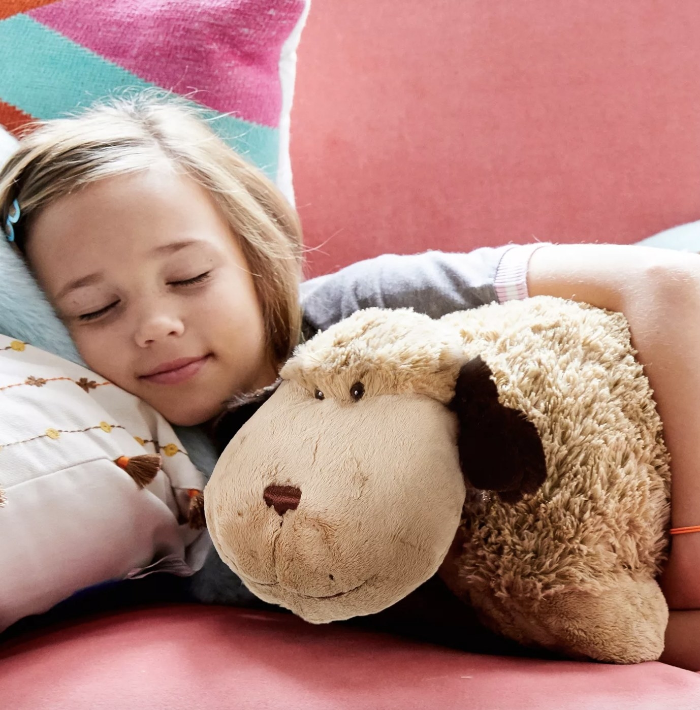 A child sleep contently next to a brown puppy pillow