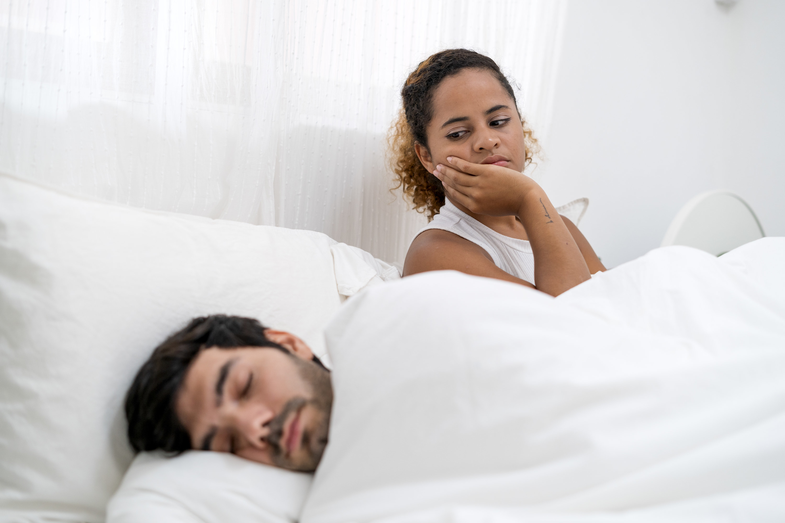 A woman staring at a man while he&#x27;s sleeping in bed