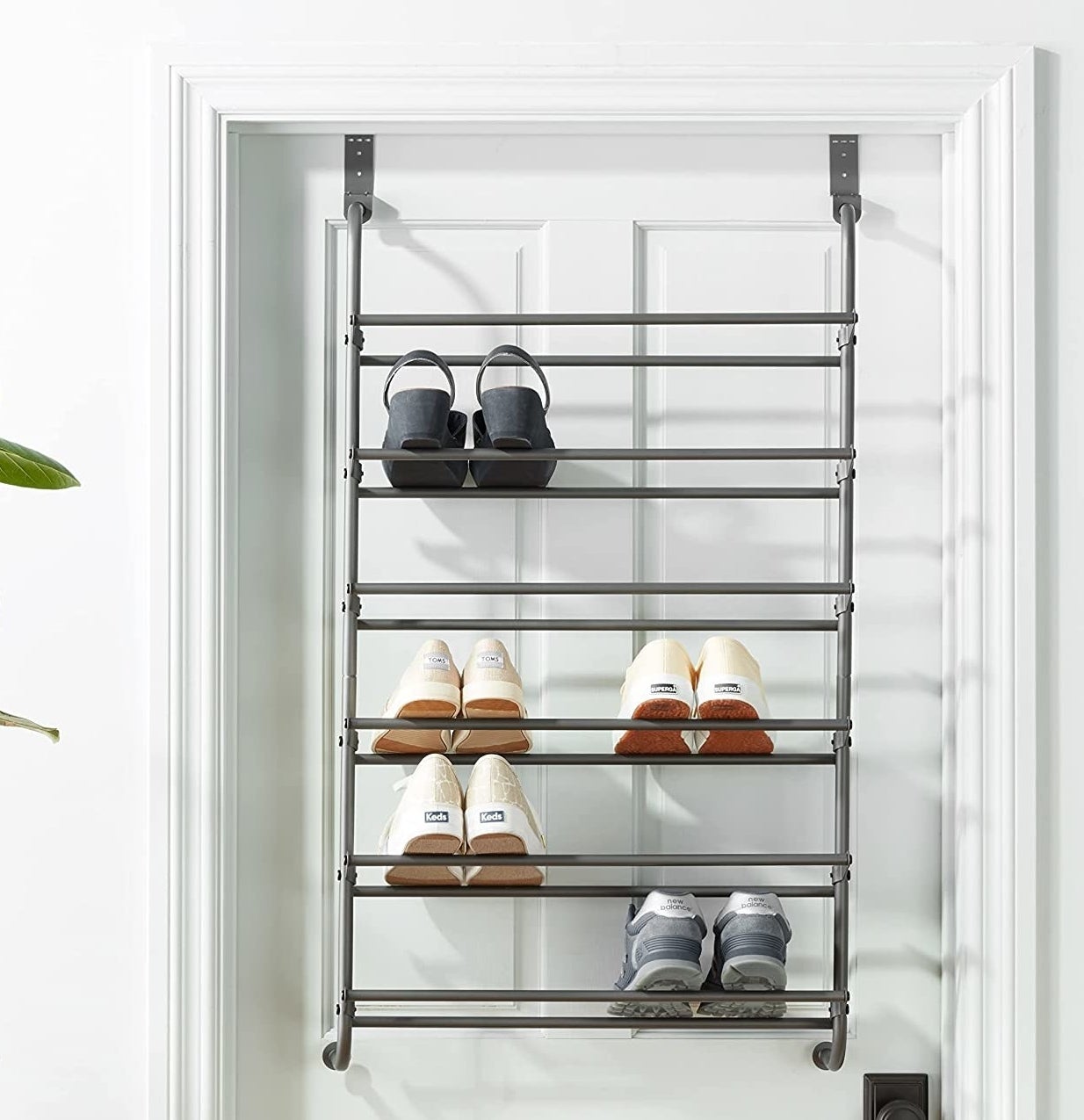 The rack hanging on a door with several pairs of shoes on it