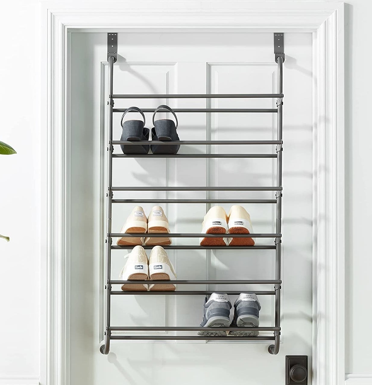 The rack hanging on a door with several pairs of shoes on it
