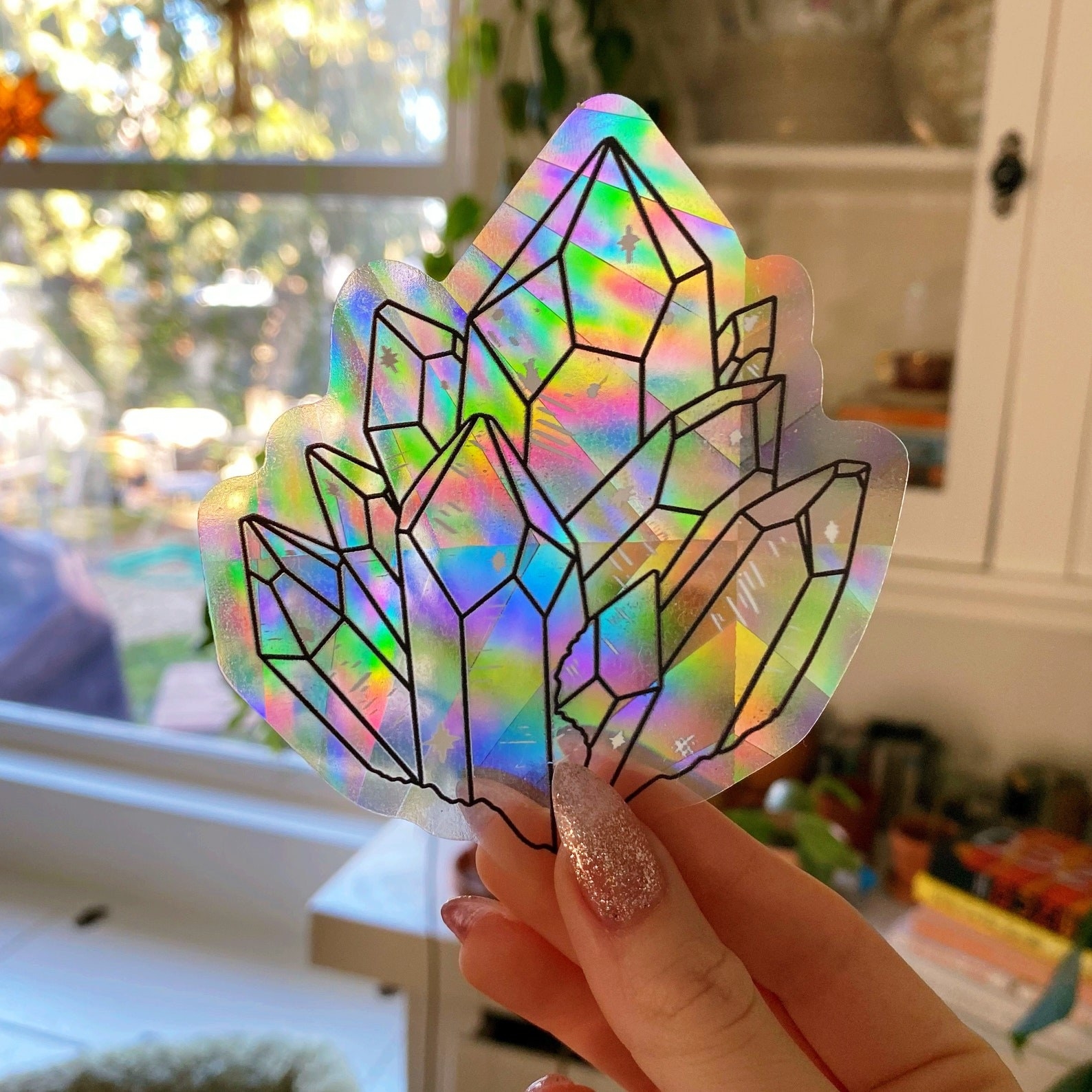 hand holds up gem-shaped shimmery sticker that&#x27;s casting off rainbows in room
