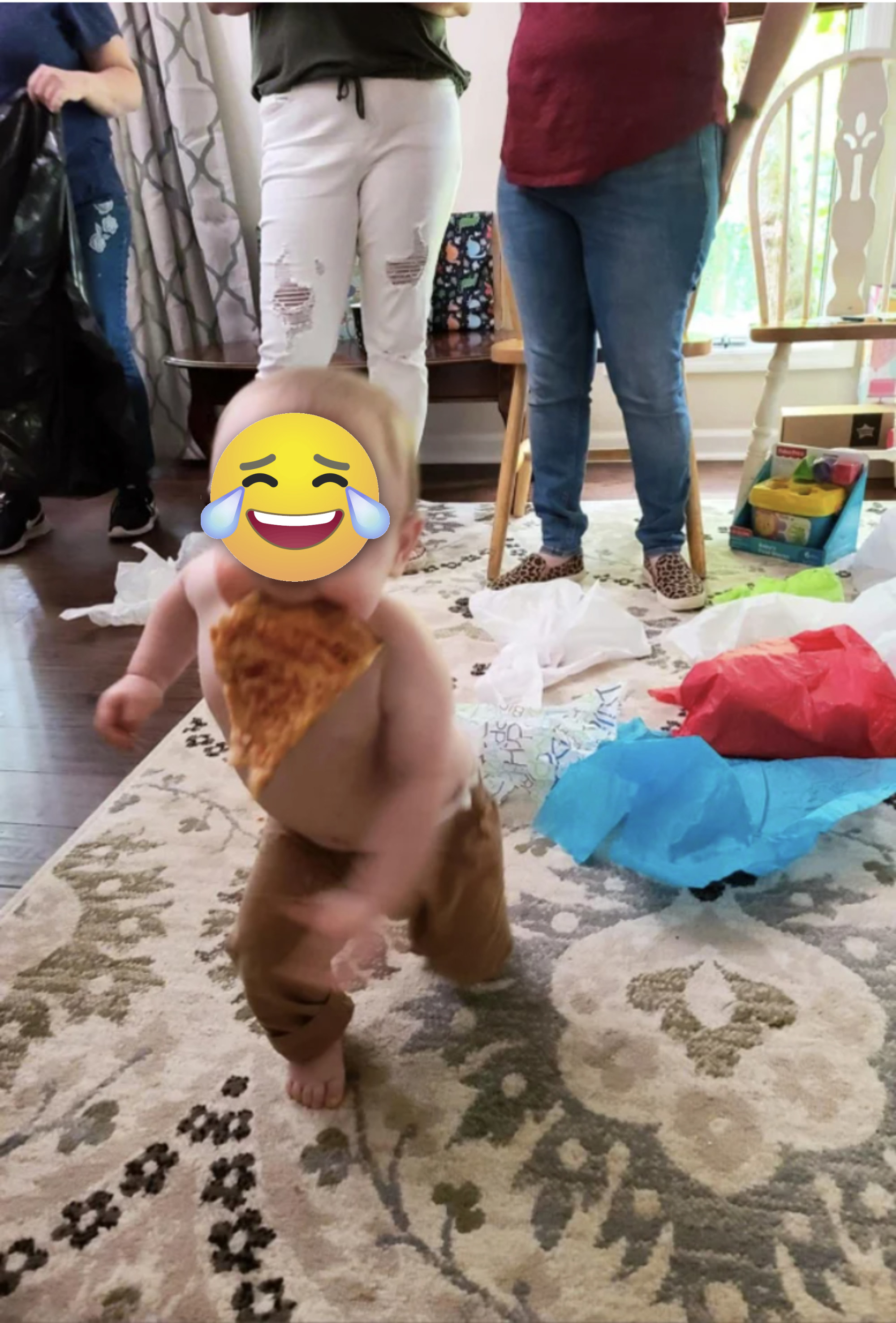 A toddler runs away with a slice of pizza in his mouth