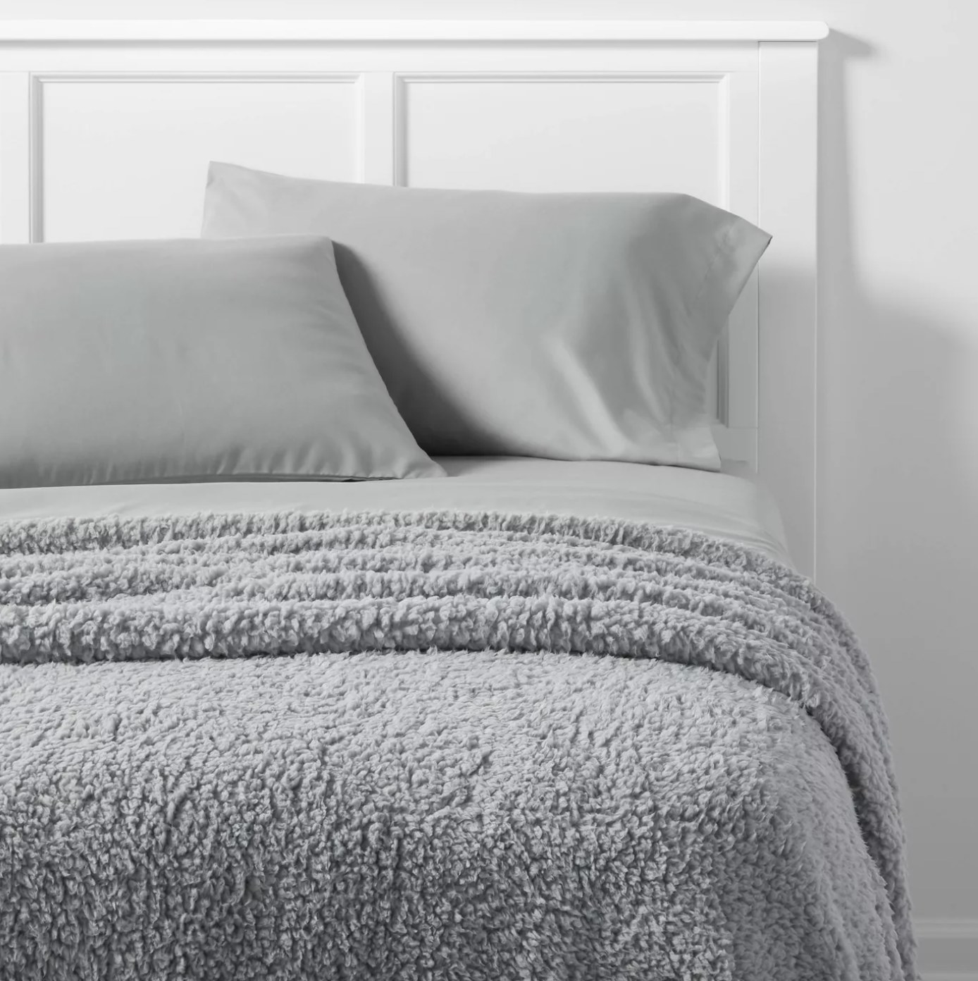 The grey sherpa blanket is on a bed with grey sheets and a white headboard