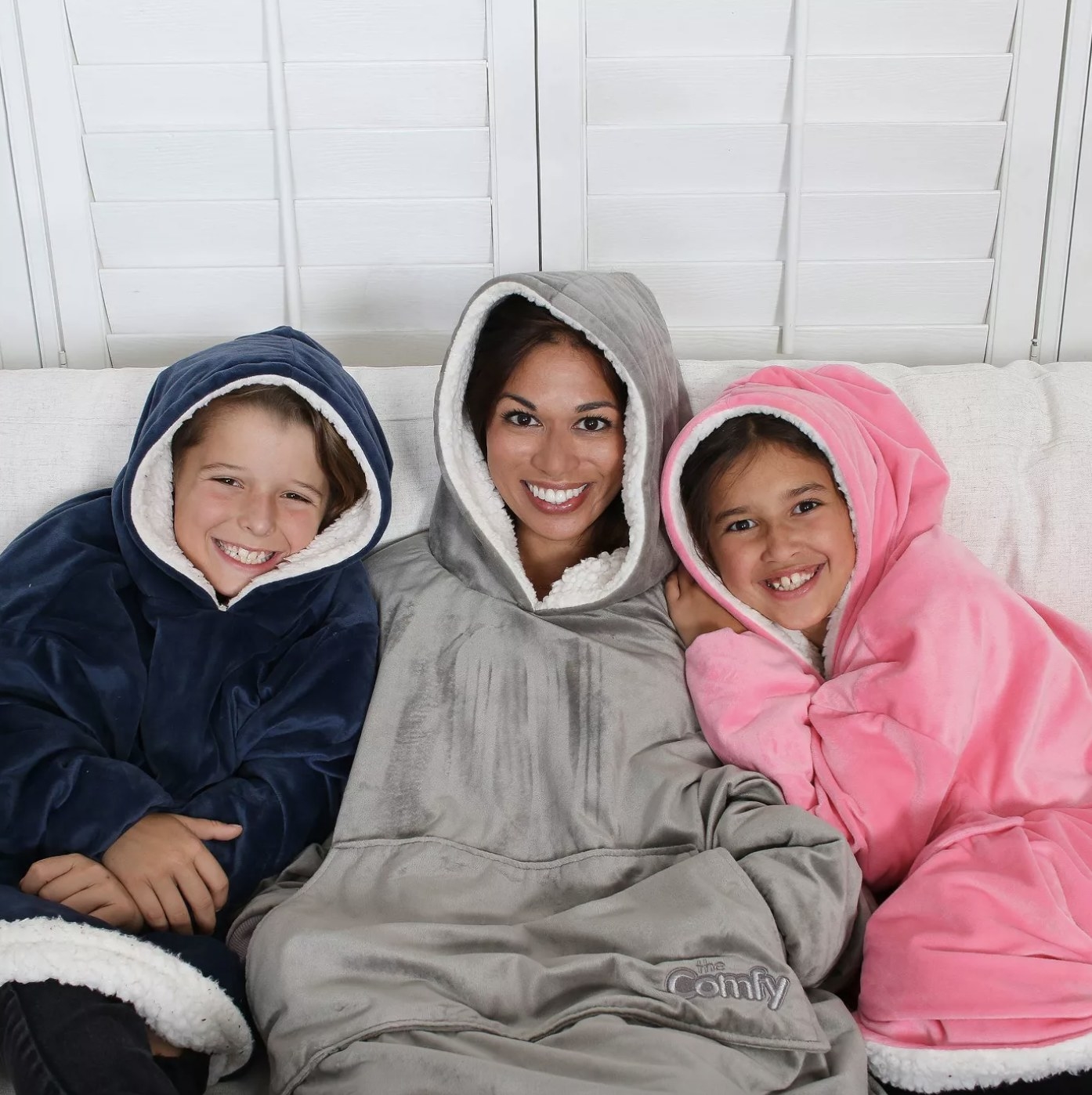 There are two children in the blanket hoodies — one blue and one pink — and one adult in a grey one