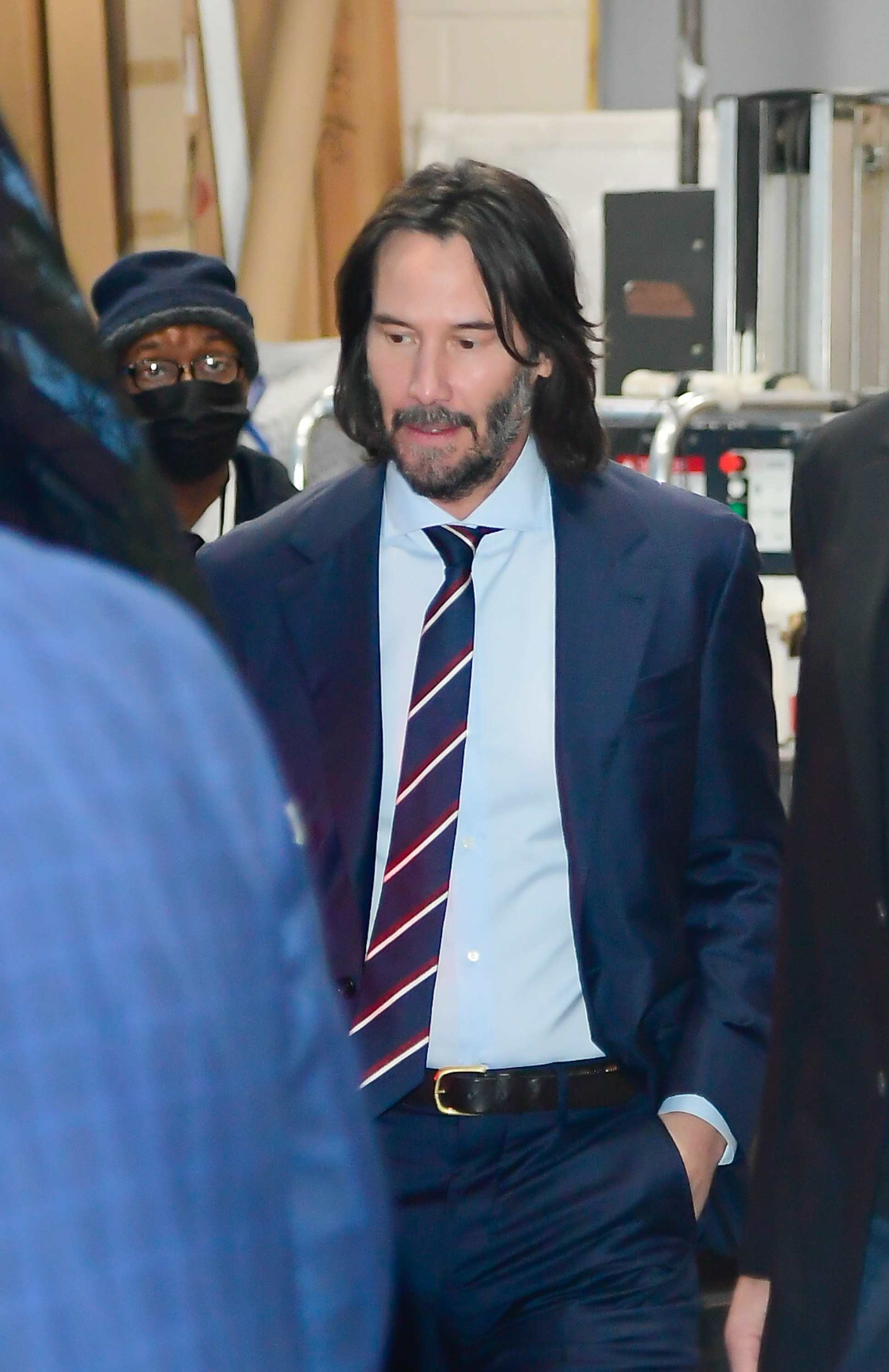 Keanu looks down while walking outside and wearing a suit and tie