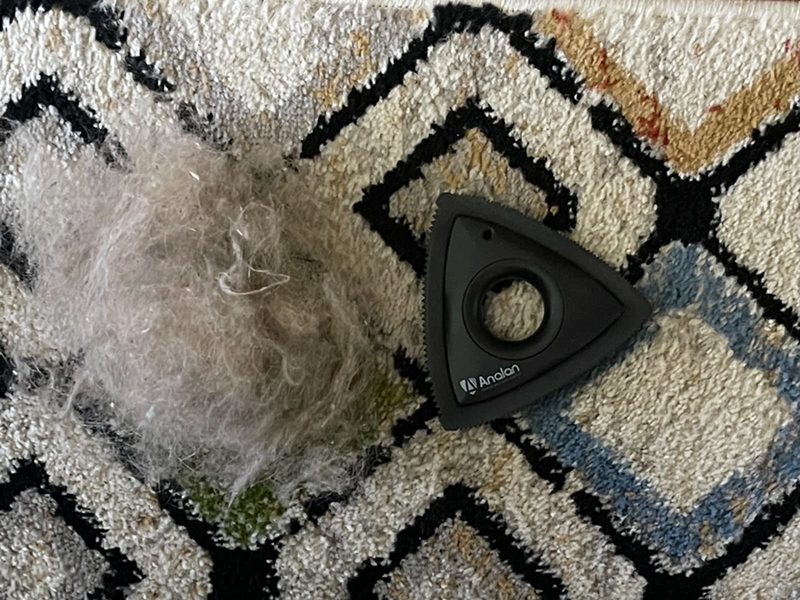 pile of gray and white fur on a carpet next the the black tool