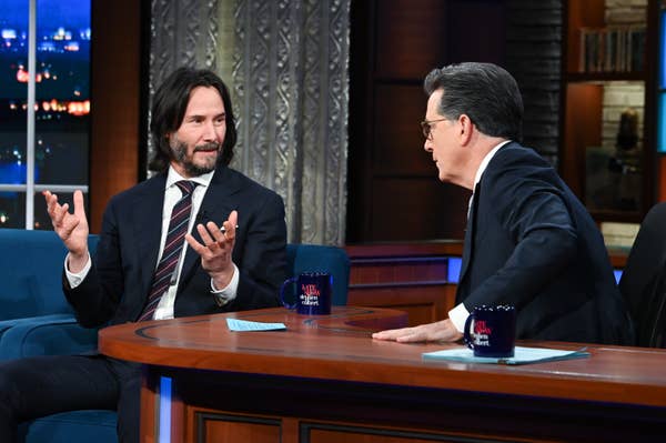 Keanu raises his hands while talking to Colbert
