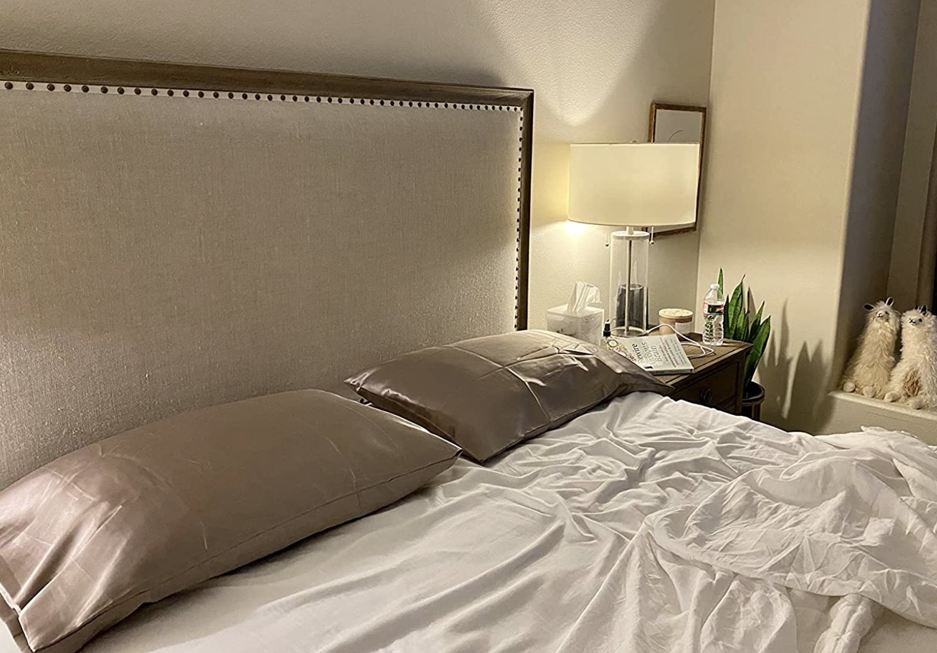 a reviewer&#x27;s satin pillowcases on two pillows on their bed