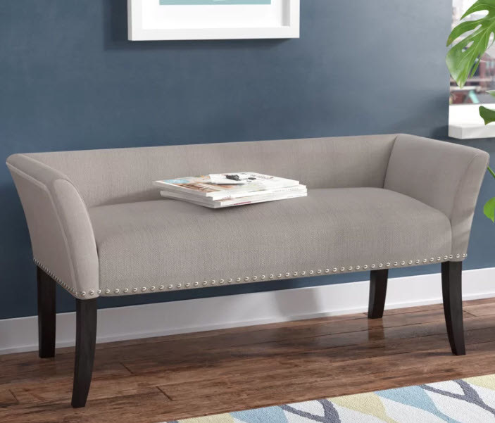An upholstered polyester compact bench with nail head trim around bottom edge