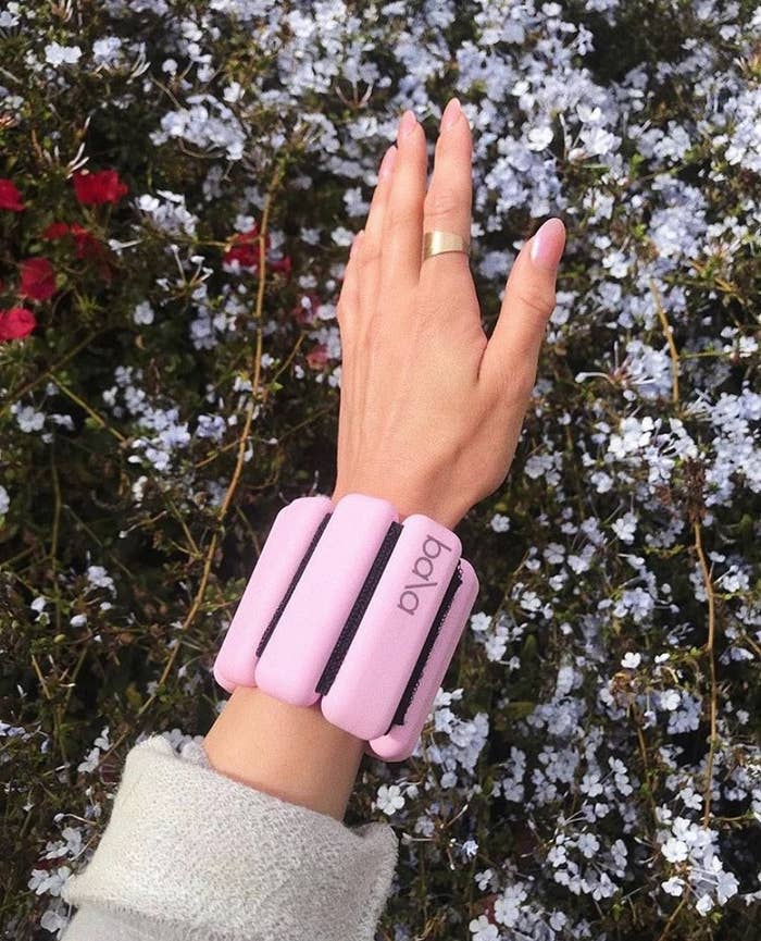 a person wearing the weighted bangle on their wrist against a floral backdrop