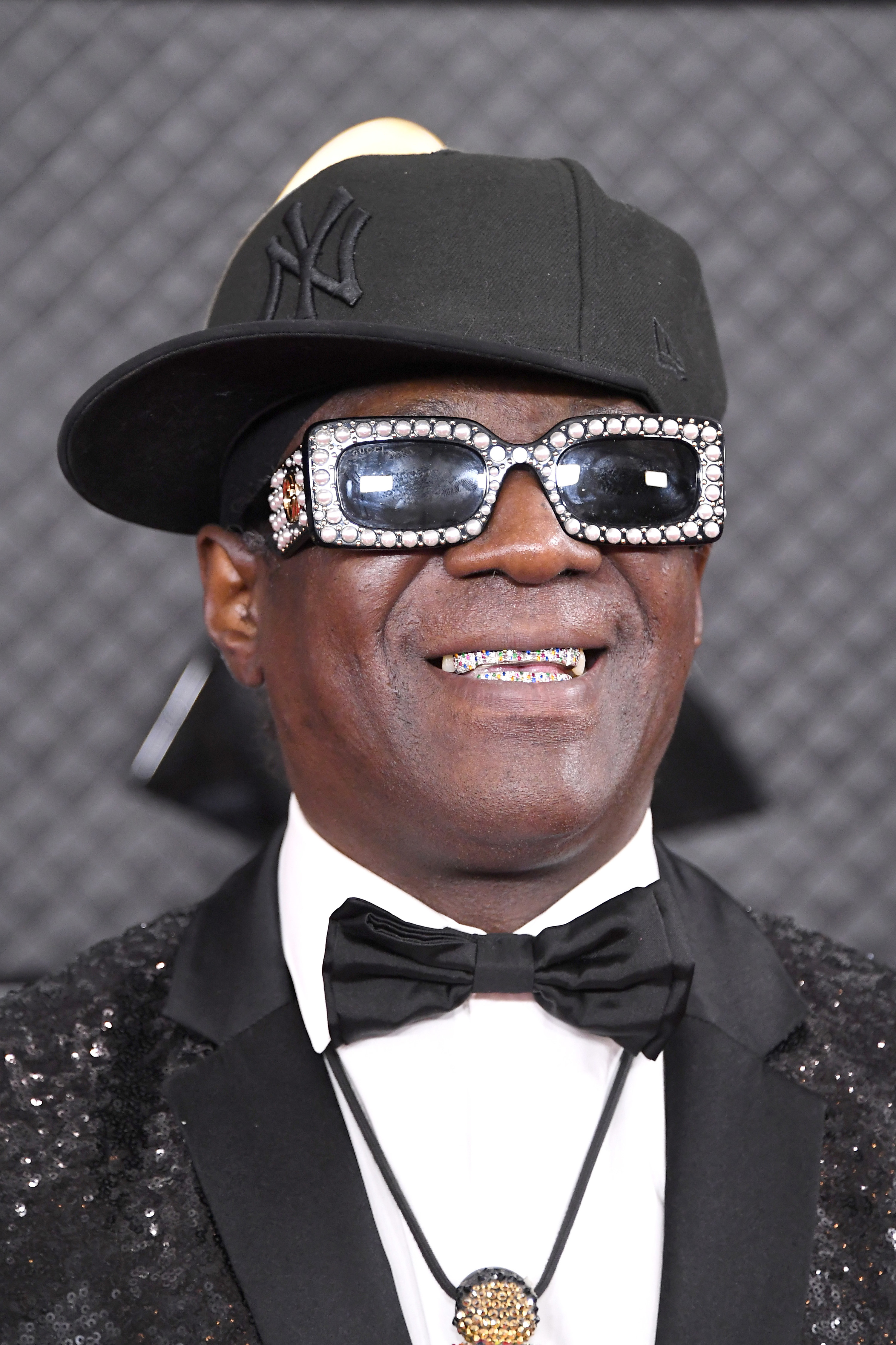 Flavor smiling at a red carpet event rocking grills and bedazzled sunglasses