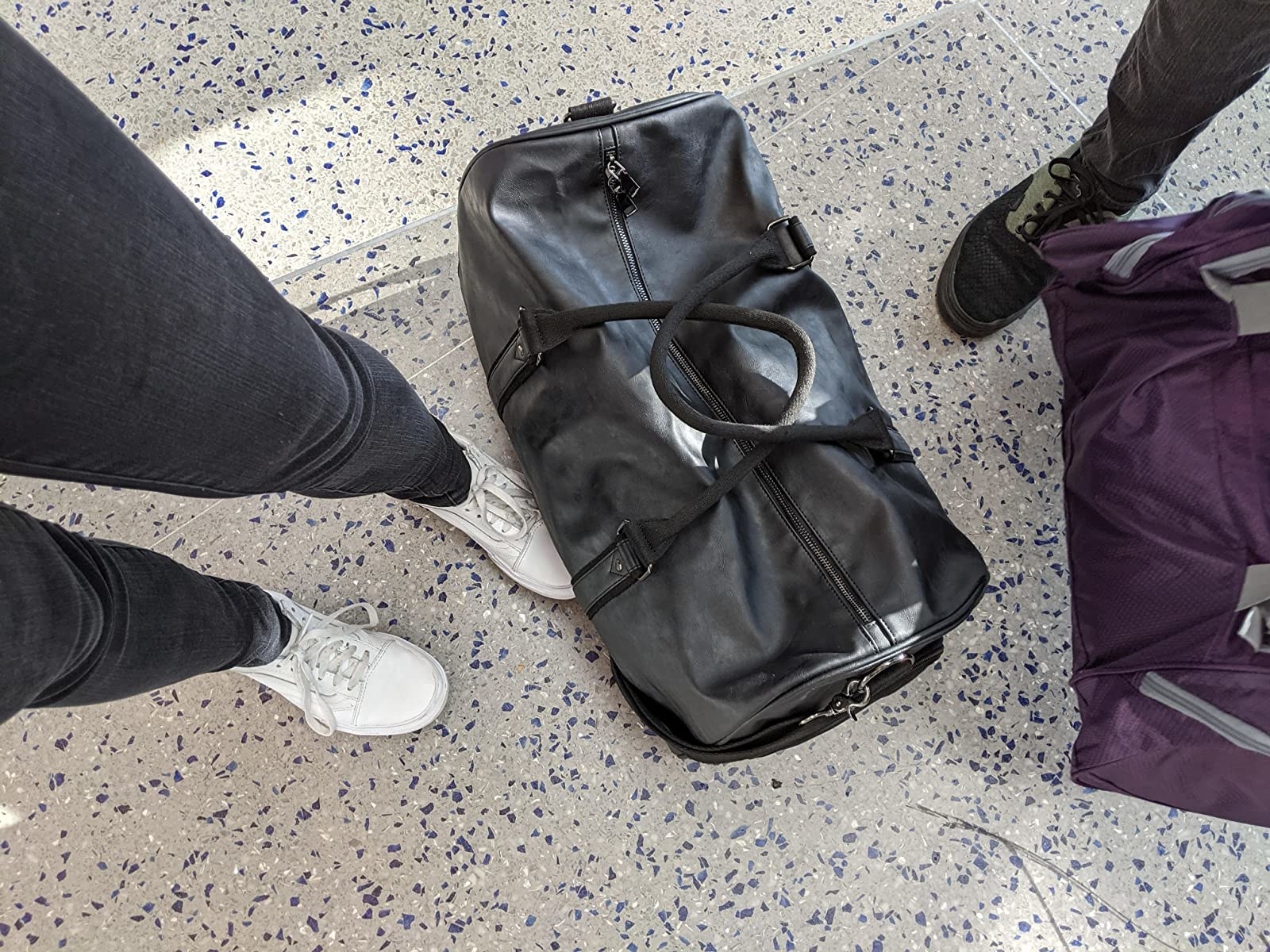 reviewer image of the black weekender bag on the ground by their feet