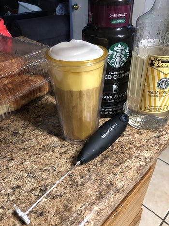 same handheld frother in front of glass filled with frothy iced coffee, milk, and vanilla syrup