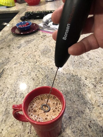 hand holds black frother mixing milk into warm hot coco