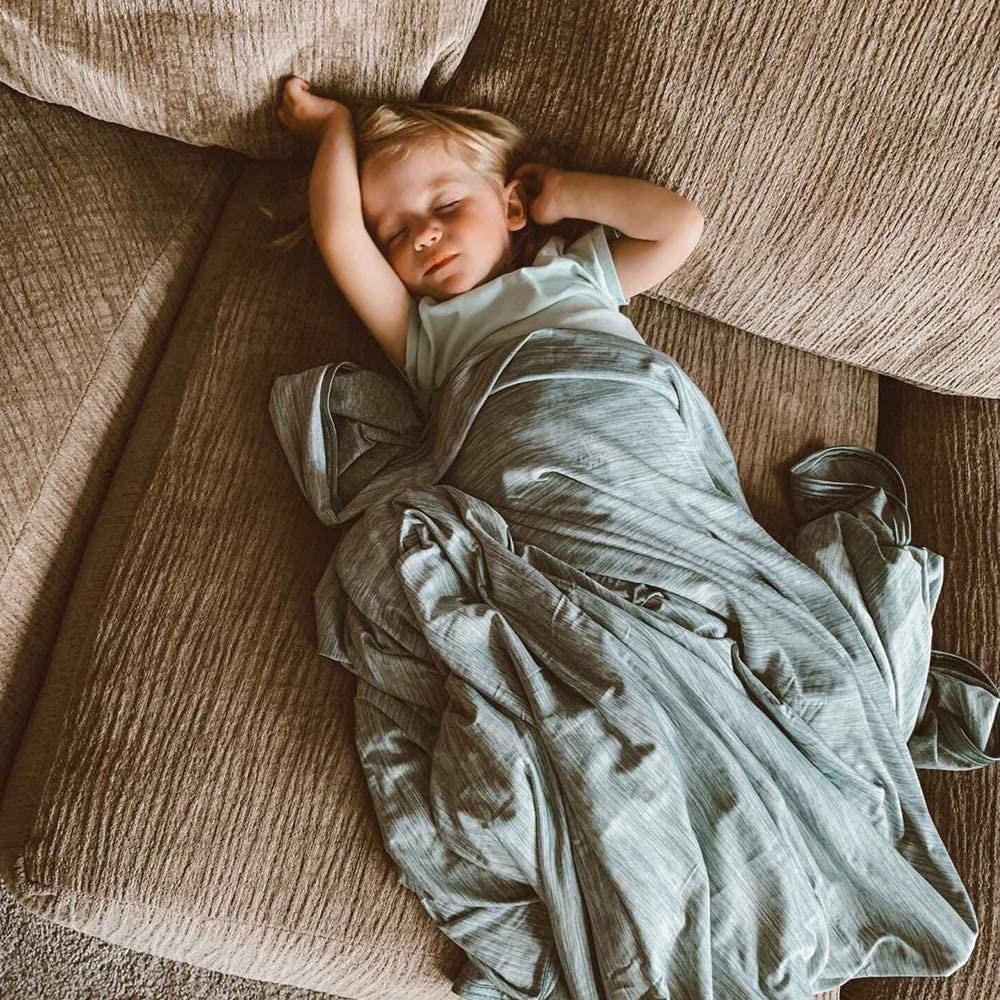 a child sleeping on a couch under the cooling blanket