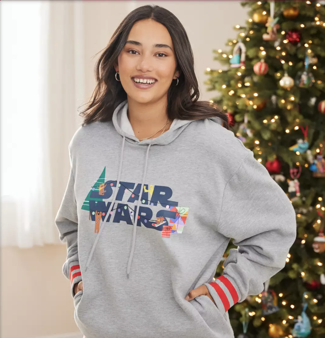 Model is wearing a grey hoodie that says Star Wars on it with some festive decor and a tree