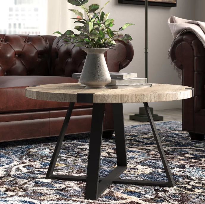 A round wooden tabletop coffee table with metal crossed legs