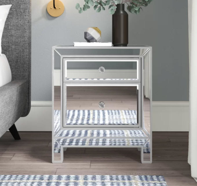 A small mirrored nightstand with a mock cabinet design and and open door
