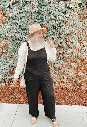 a reviewer wears the black jumpsuit with a shirt underneath and a beige hat