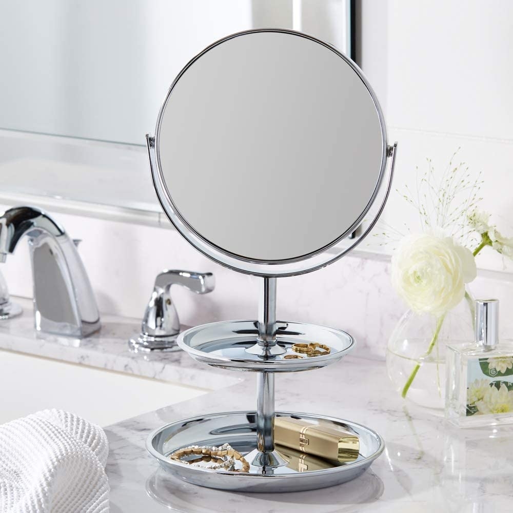 The mirror on a bathroom counter with jewellery and a lipstick in its trays